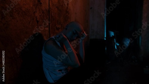 A bald woman who is a drug addict feels withdrawal symptoms without drugs. Old basement in neon light. Hopeless drug addict photo
