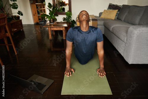 Young African man doing the cobra pose during yoga at home photo