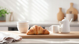 Freshly baked croissant is presented on a plate next to a white coffee mug and a small bowl of nuts, all arranged on a wooden table with a warm, inviting light.
