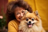 Middle aged woman in yellow sweater with long brown hair holds an puppy and smiles on the yellow background