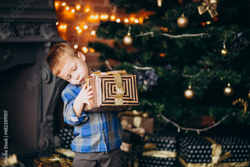 Little cute boy with christmas gift by Christmas tree photo