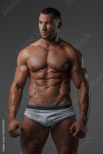 Portrait of a rugged man with a well-groomed model appearance  wearing white briefs  and showcasing his bare muscular torso against a gray background