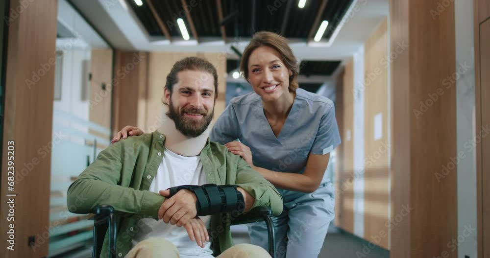 Portrait of happy injured Caucasian man recovering in hospital with qualified female doctor looking at camera and smiling. Bearded young patient and helpful nurse in modern clinic. Portrait of happy injured Caucasian man recovering in hospital with qualified female doctor looking at camera and smiling. Bearded young patient and helpful nurse in modern clinic.