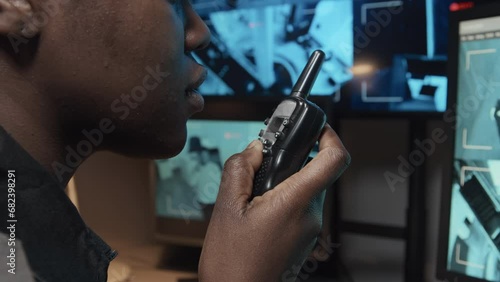 Closeup side shot of security officer talking on handheld transceiver while monitoring CCTV video footages on multiple monitors in surveillance room photo