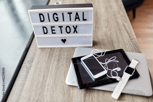 technology concept - digital detox words on light box and different gadgets on blue background