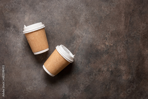 Coffee in paper cups lay flat on a dark brown background. View from above. Disposable tableware. Take-out drinks