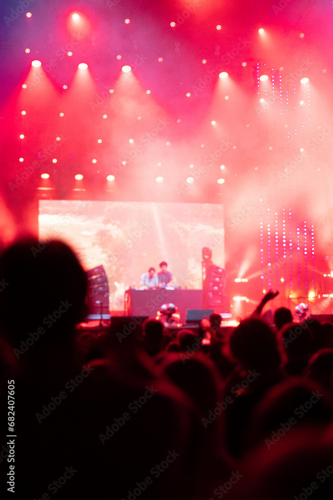 Large concert. Smoke effects and large red bright display screen on stage. Audience cheering and dancing