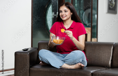 Indian young female watching tv with snack bowl in hand at home