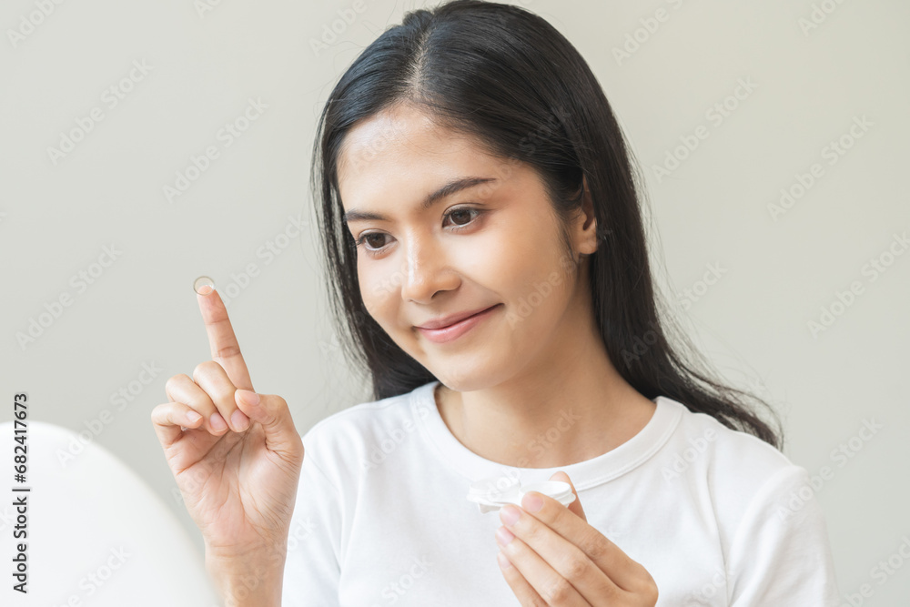 Ophthalmology care, eye sight, vision concept, happy asian young woman, female holding and putting soft contact lenses with finger on face from box case, looking in mirror at home. Medicine and health Ophthalmology care, eye sight, vision concept, happy asian young woman, female holding and putting soft contact lenses with finger on face from box case, looking in mirror at home. Medicine and health