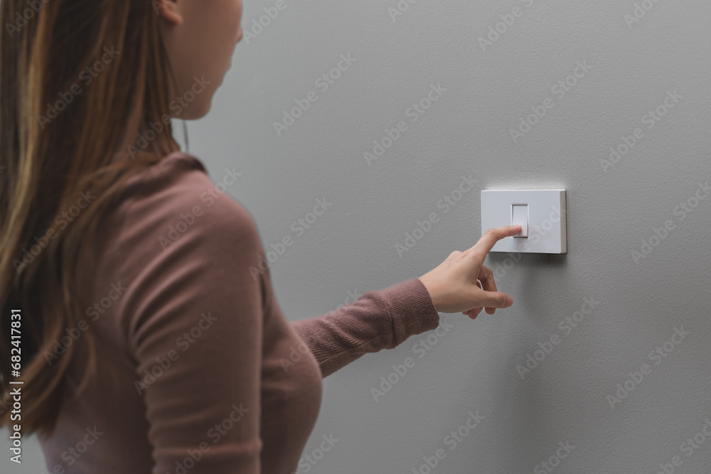 Asian young woman hand turn off on lighting switch at home room. Finger ...