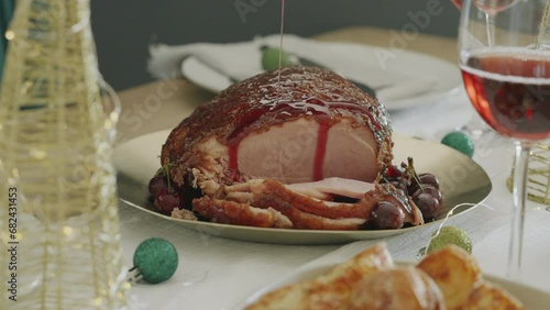 Medium close-up clip of a Christmas Gammon on a decorated xmas dinner or lunch table. Sliced glazed ham and beautiful woman pouring cherry glaze over the meal. Home cooked festive family meal.