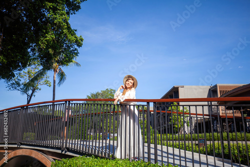 Resort lifestyle. Woman in hat enjoying sunny day on hotel bridge surrounded by tropical trees. Luxury holiday.
