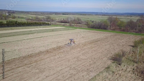 A farmer on a tractor with a seeder sows grain in plowed land in a private field in the village area. Mechanization of spring field work. Farmer's everyday life. Processing of land. The agrarian
