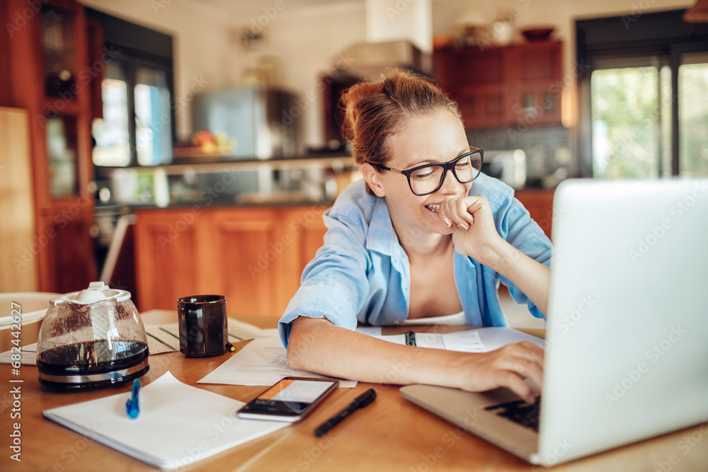 Smiling young woman in casual clothing using laptop working from home Smiling young woman in casual clothing using laptop working from home