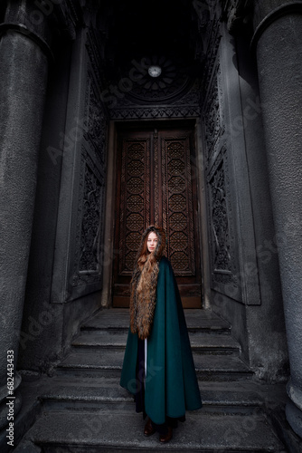 Fairytale princess wearing cloak with medieval castle door on the background. © luengo_ua