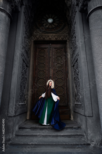 Fairytale princess wearing cloak with medieval castle door on the background. © luengo_ua