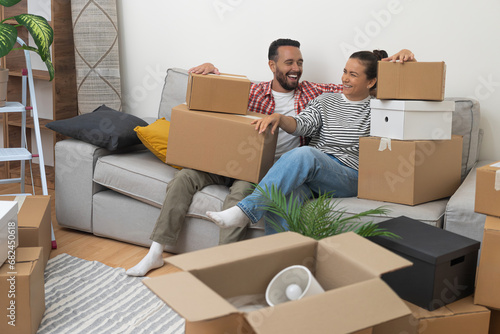 Positive couple of adult man and woman rejoice at new purchase of apartment sitting on sofa with stacks of packed boxes with things for moving in living room photo