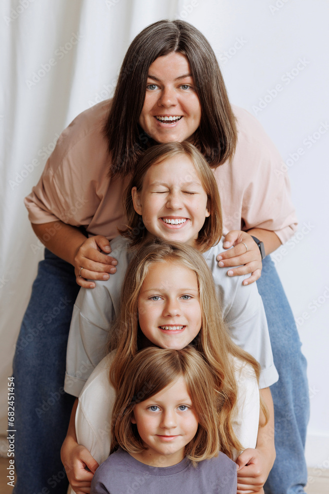 Four girls in casual clothes smile and hug in front of a white wall. Concept for demonstrating family love, friendship and happiness. Faces in a row. Four girls in casual clothes smile and hug in front of a white wall. Concept for demonstrating family love, friendship and happiness. Faces in a row.