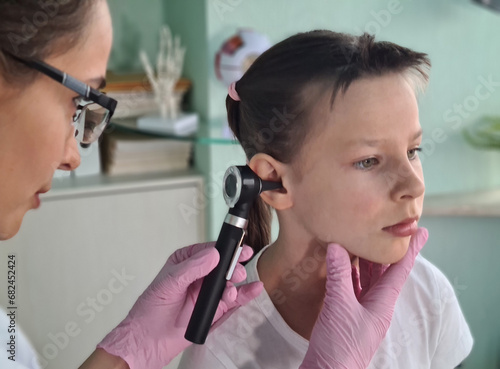 Caring therapist checks ear canal of little girl with professional medical otoscope