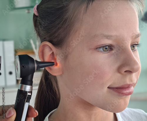 Otorhinolaryngologist examines little girl ear with otoscope photo