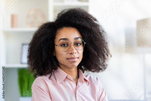 Close-up photo of a young African-American businesswoman in a pink shirt looking seriously and confidently into the camera.