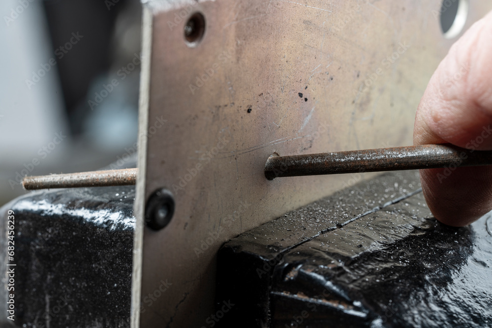 Craftsman works on small piece of metal with round metal file gripped ...