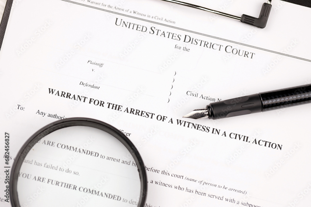 District court warrant for the arrest of a witness in a civil action papers on A4 tablet lies on office table with pen and magnifying glass close up District court warrant for the arrest of a witness in a civil action papers on A4 tablet lies on office table with pen and magnifying glass close up