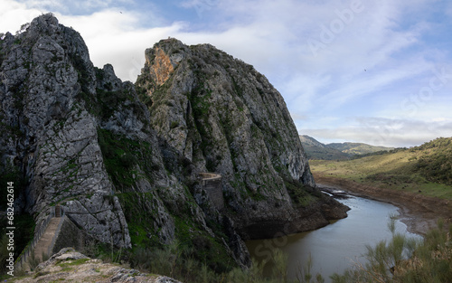 Scenic view of a the Hundidero Dam and river winding through a rocky mountain landscape under a cloudy sky.