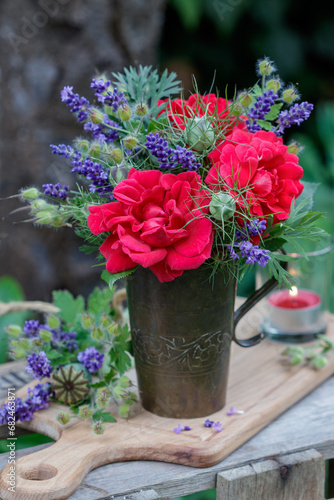 Blumenstrauß mit roten Rosen und Lavendelblüten im alten Kupferbecher im Garten