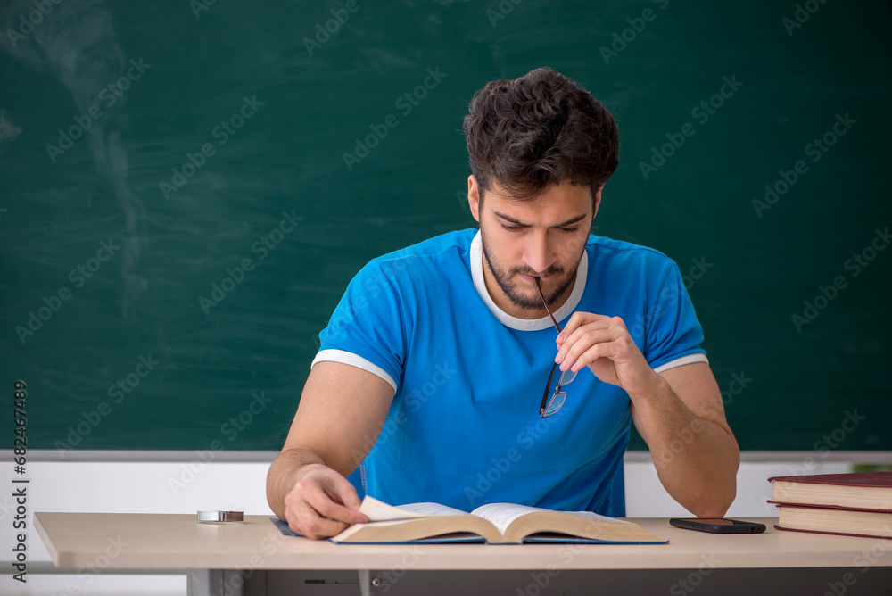 Young male teacher student in front of green board