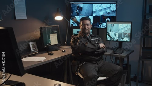 Portrait of smiling male Biracial security officer controlling surveillance CCTV video footage on multiple monitors and then turning to camera in guard room photo