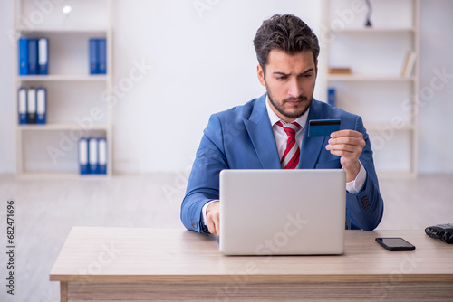 Young male employee holding credit card at workplace