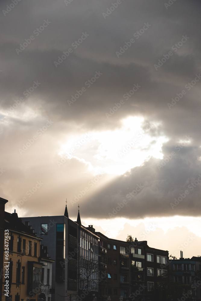 Sun breaks through the clouds at sunset and sends its rays towards buildings in Kortrijk, Belgium