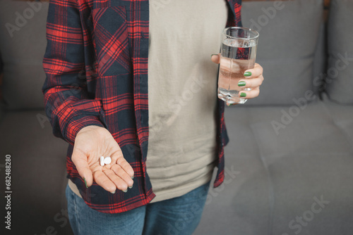 Young woman taking medicine, holds in a hand white pills and glass of water, close-up view