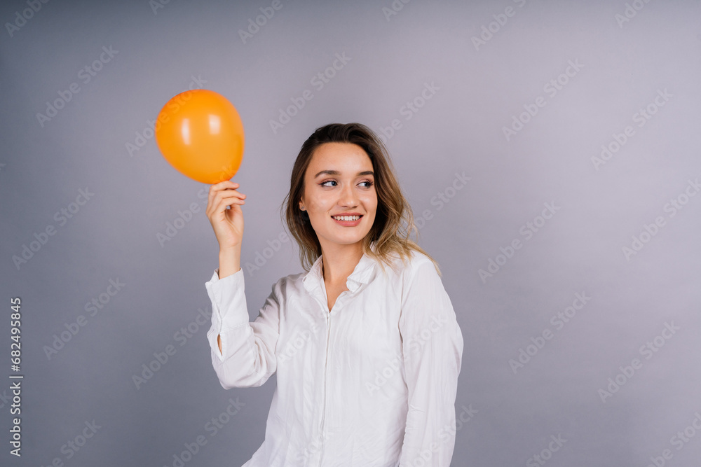 Close up portrait of a young woman inflating balloon on isolated grey background Close up portrait of a young woman inflating balloon on isolated grey background