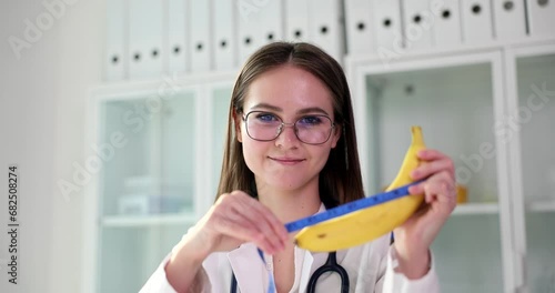 Doctor woman urologist holds a banana and measuring tape in hands. Erectile dysfunction and weak erection