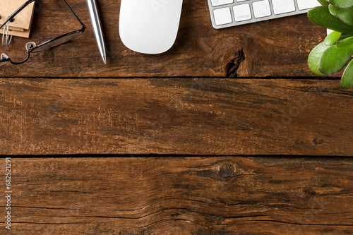 Modern office desktop. Computer keyboard with mouse, notebook, eyeglasses and green flower on wooden background with copyspace. Top view