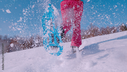 CLOSE UP, LOW ANGLE VIEW: Active lady runs up the snowy hill in blue snowshoes