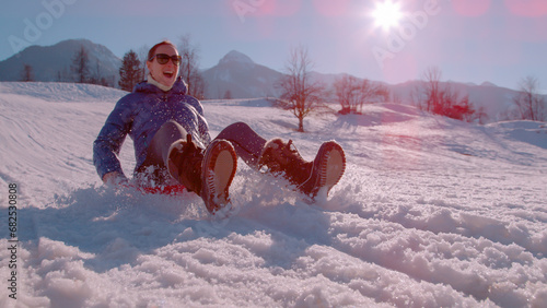 CLOSE UP, LENS FLARE: Sunny winter day with a lady sledding down the snowy hill photo