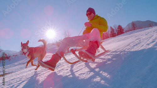 Foto CLOSE UP, LENS FLARE: Cheerful man sledding and brown dog running by his side