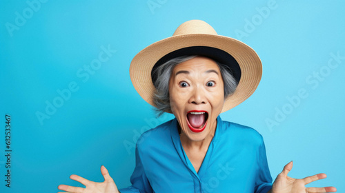 Middle age senior asian woman wearing blue hat and denim shirt standing over pink background surprised and amazed with open mouth for success, raised raised arms with.