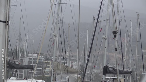 The masts of sailing boats are bobbing in the rain in the port. Slow motion.