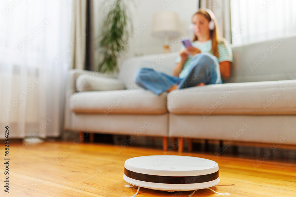 A woman in headphones sits on couch while a robotic vacuum cleaner does cleaning A woman in headphones sits on couch while a robotic vacuum cleaner does cleaning