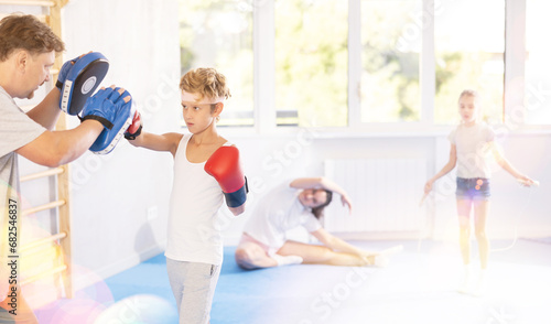 Young boy with her trainer father at gym. Boy wearing boxing gloves exercise and punch to pads for boxing