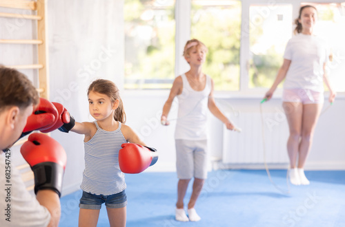 Girl and dad are boxing in gym, father helps daughter child to work out force of blow. Modern positive family chooses active hobby