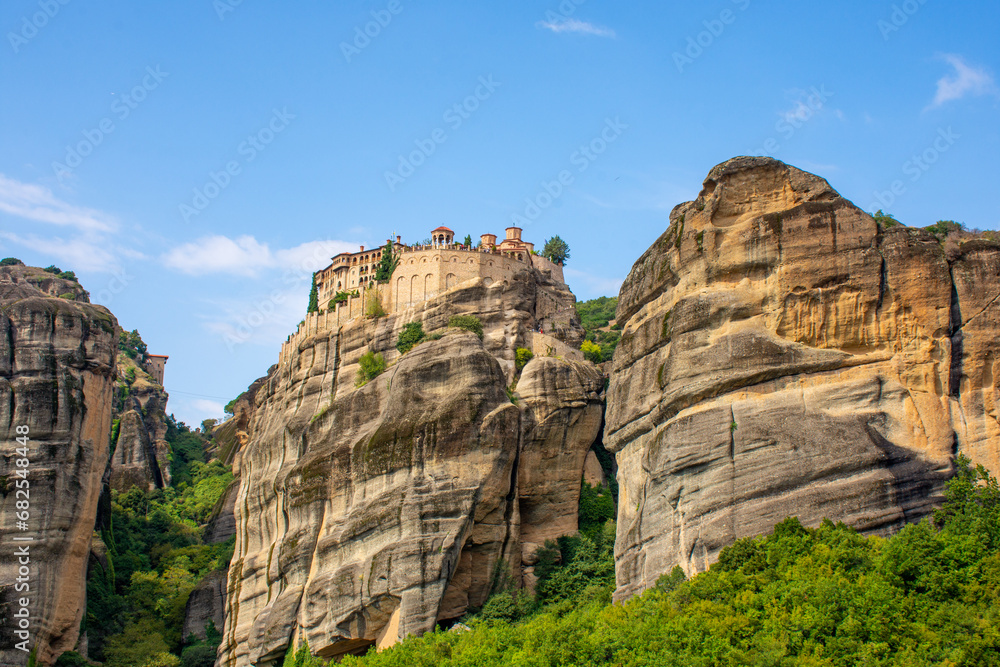 morning view of Meteora Monastery complex on rocks, illuminated by rising sun against mountains in background. UNESCO World Heritage Site. Greece.
