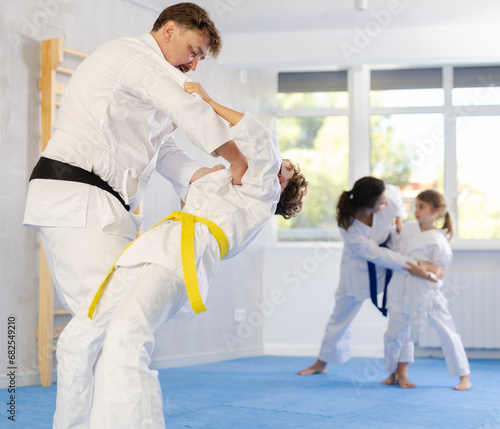 Family training moment. Focused determined preteen boy in white kimono sparring with experienced father mentoring tween son in martial arts in gym