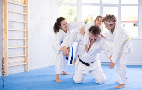 Family frolic in gym after active martial arts class. Children and woman jokingly attack father of family, doing rough-and-tumble
