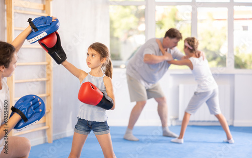 Little girl in boxing gloves learns to box from the punch mitts of her mom trainer in the gym