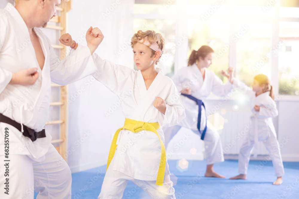 Fototapeta premium Family training moment. Focused determined preteen boy in white kimono sparring with experienced father mentoring tween son in martial arts in gym